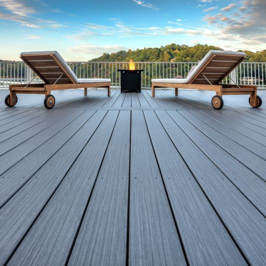 Two wooden lounge chairs on a gray deck with a small fire pit, overlooking a scenic view.