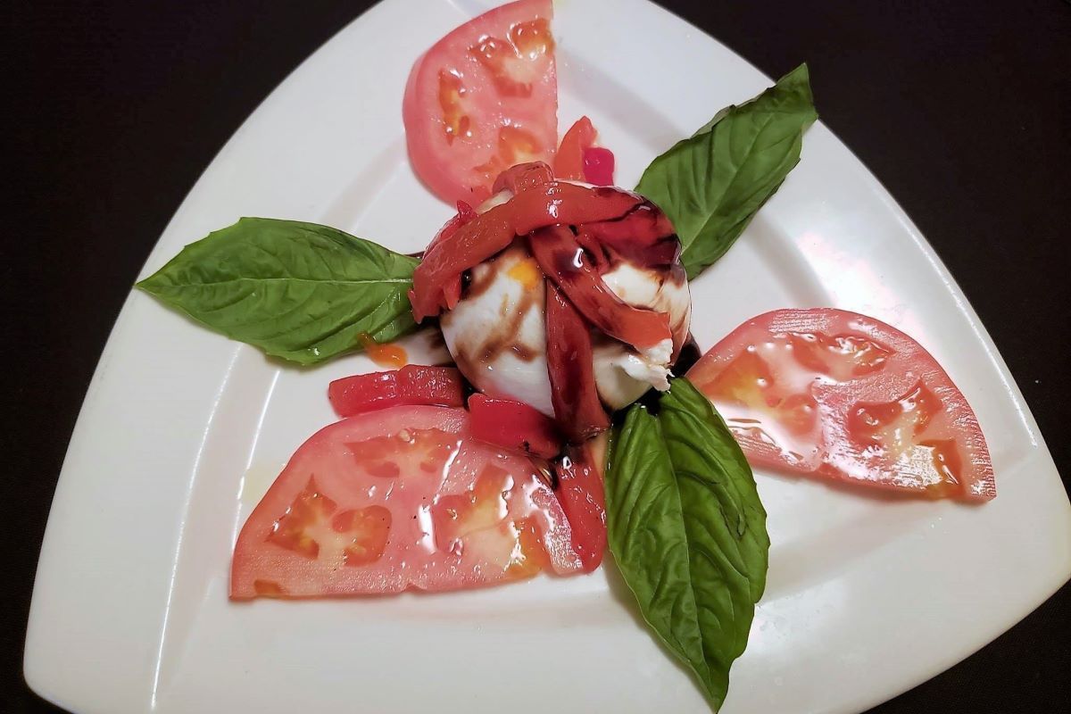 A white plate topped with fresh burrata, sliced tomatoes and basil