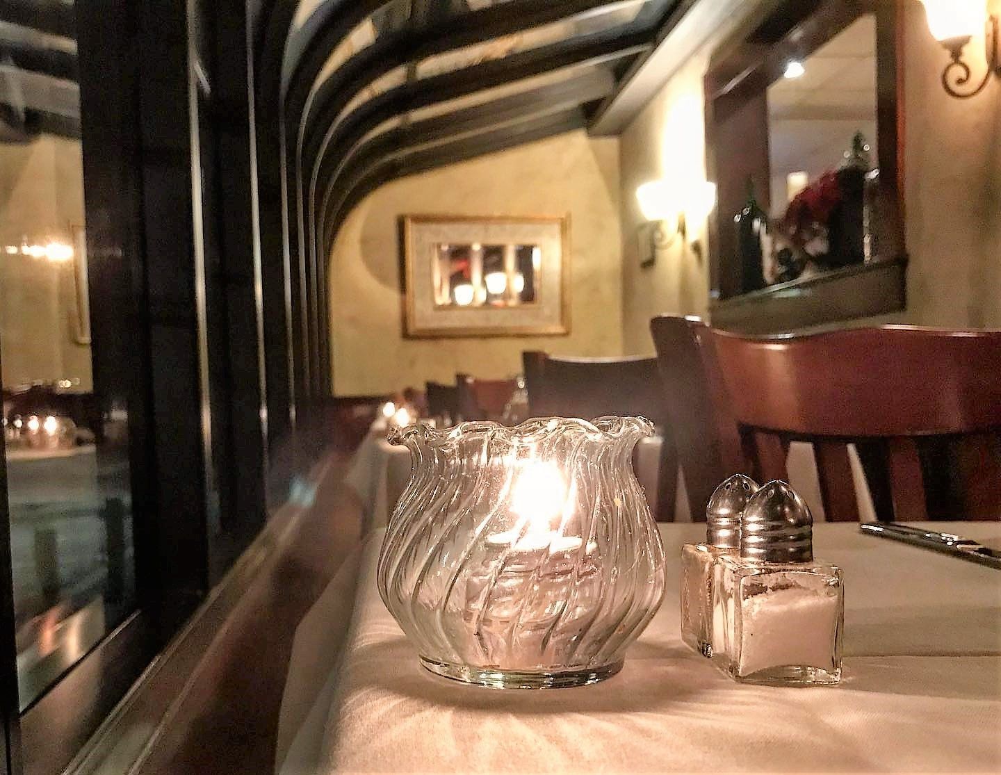 A glass candle holder sits on a table next to a salt and pepper shaker