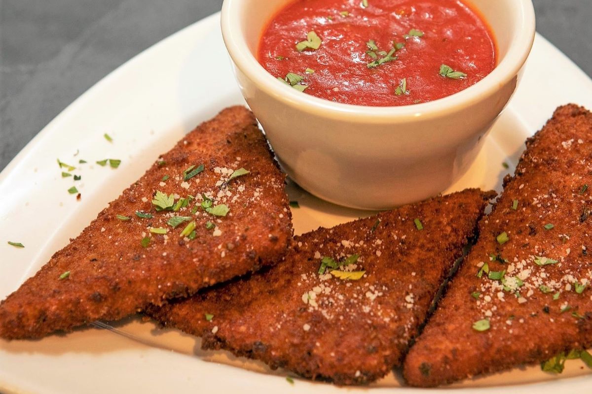 A white plate topped with fried mozzarella cheese and a bowl of marinara.