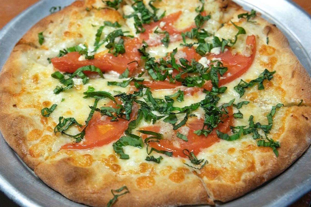 A margherita pizza with tomatoes, mozzarella cheese and basil on a metal pan.