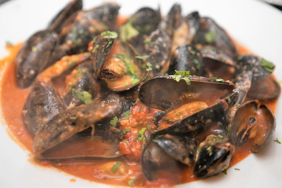 A close up of a plate of mussels in red sauce on a table.