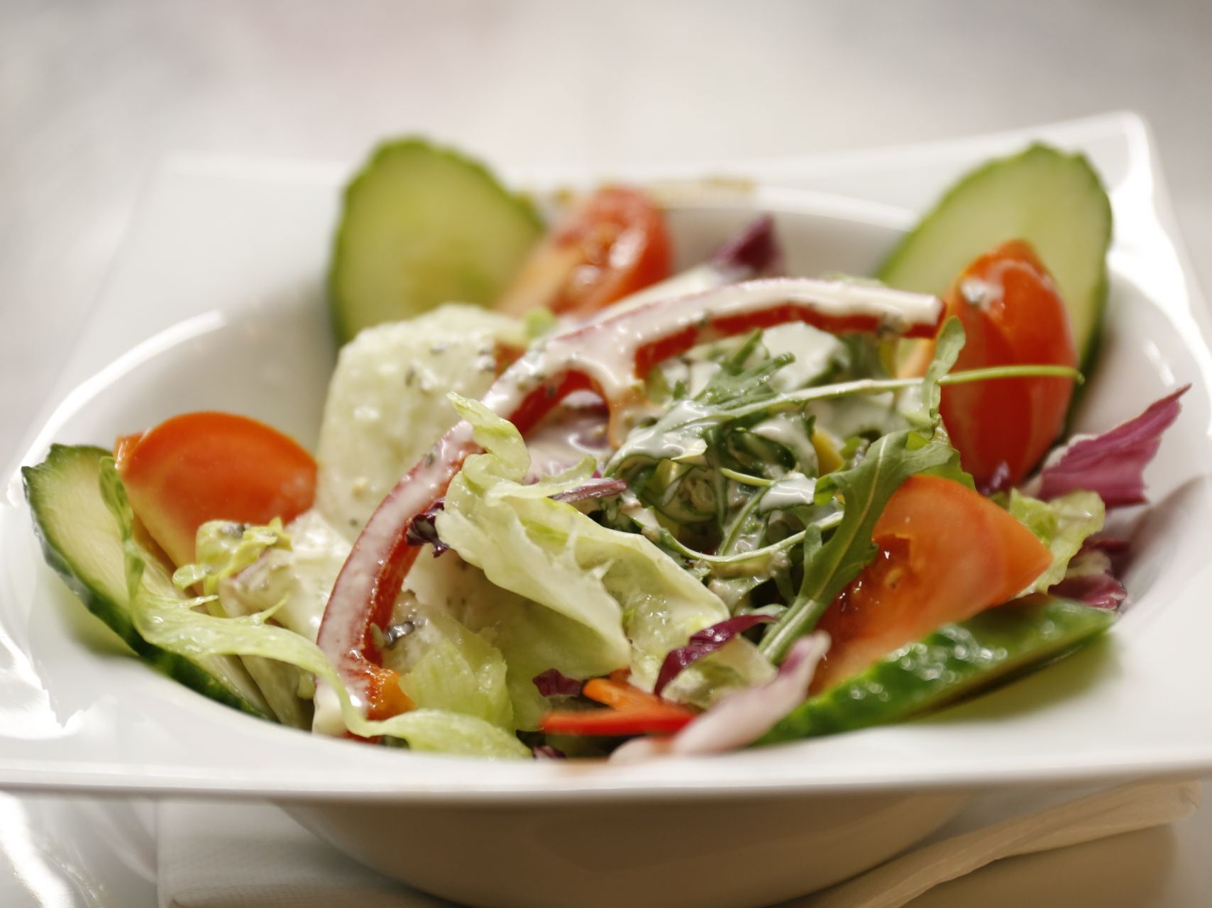 A white bowl filled with a salad of lettuce, tomatoes , cucumbers and red pepper with an Italian dressing.