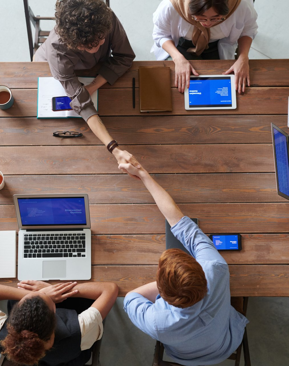 An overview of four employees at a table while two shake hands