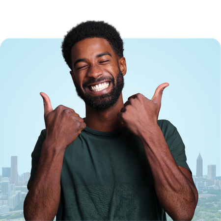 Man with a beard giving two thumbs up, smiling with city skyline in the background.