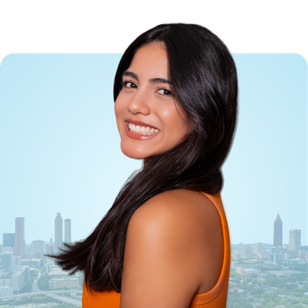 Woman smiling, looking over shoulder, against a city skyline background. She's wearing an orange top.