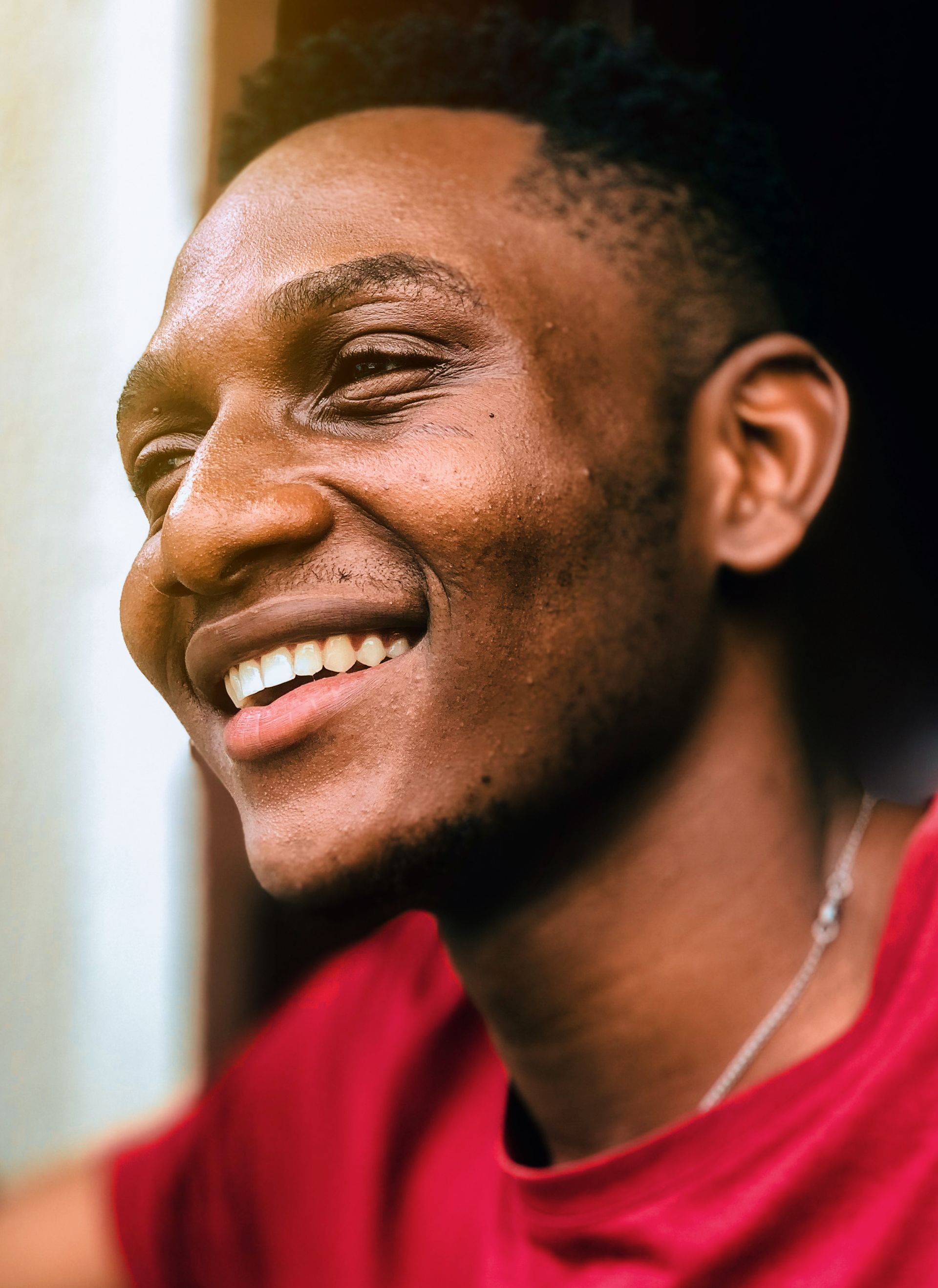 Smiling person in a red shirt, looking off to the side in soft natural light