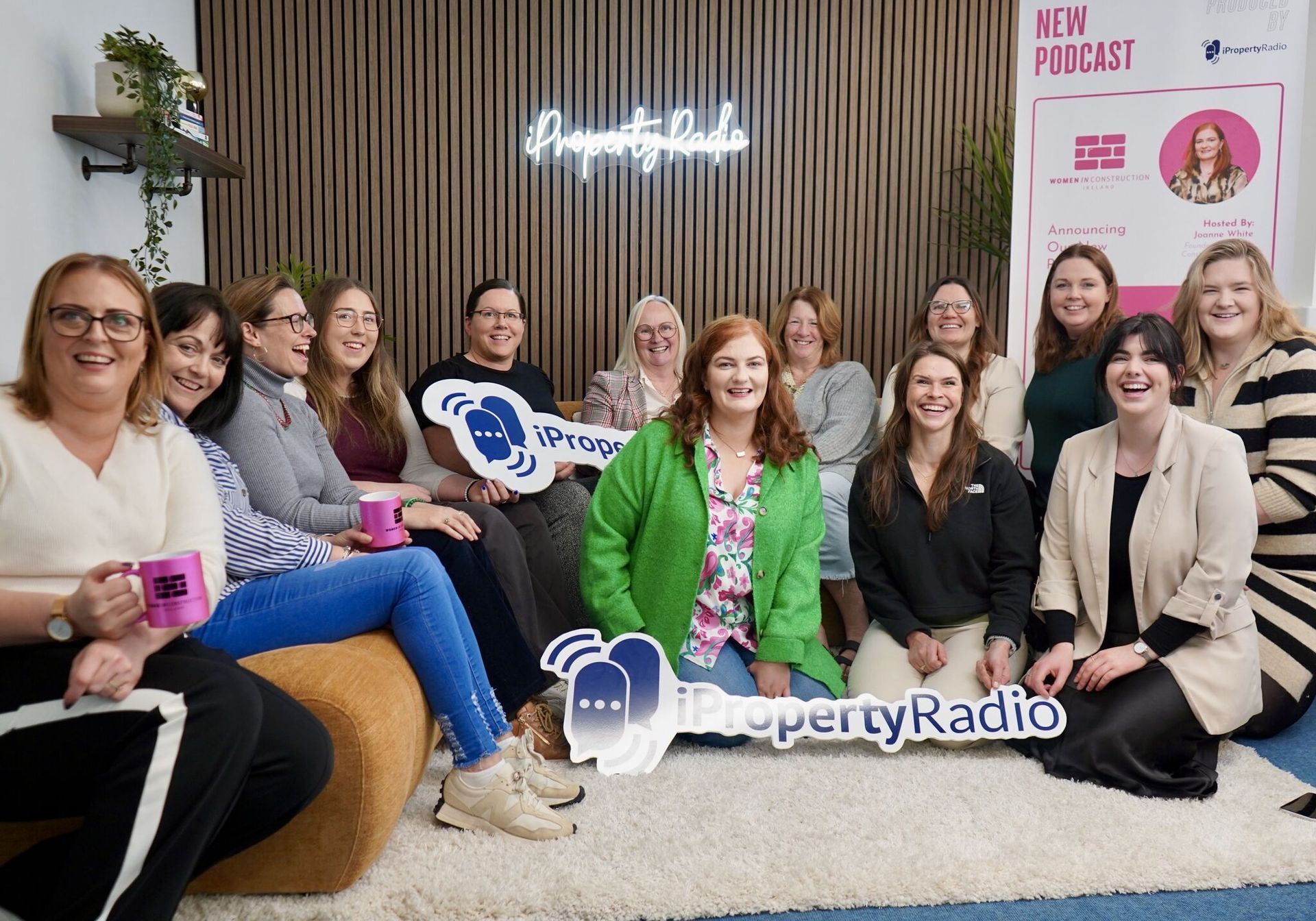 Group seated in a studio, smiling for Property Radio with neon sign and podcast banner behind them