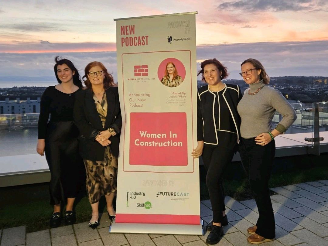 Four people posing beside a “Women in Construction” banner at sunset overlooking a city.