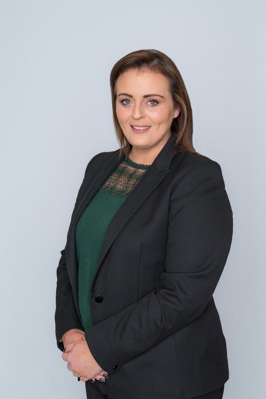 Professional portrait of a woman in a black blazer and green top against a light gray background