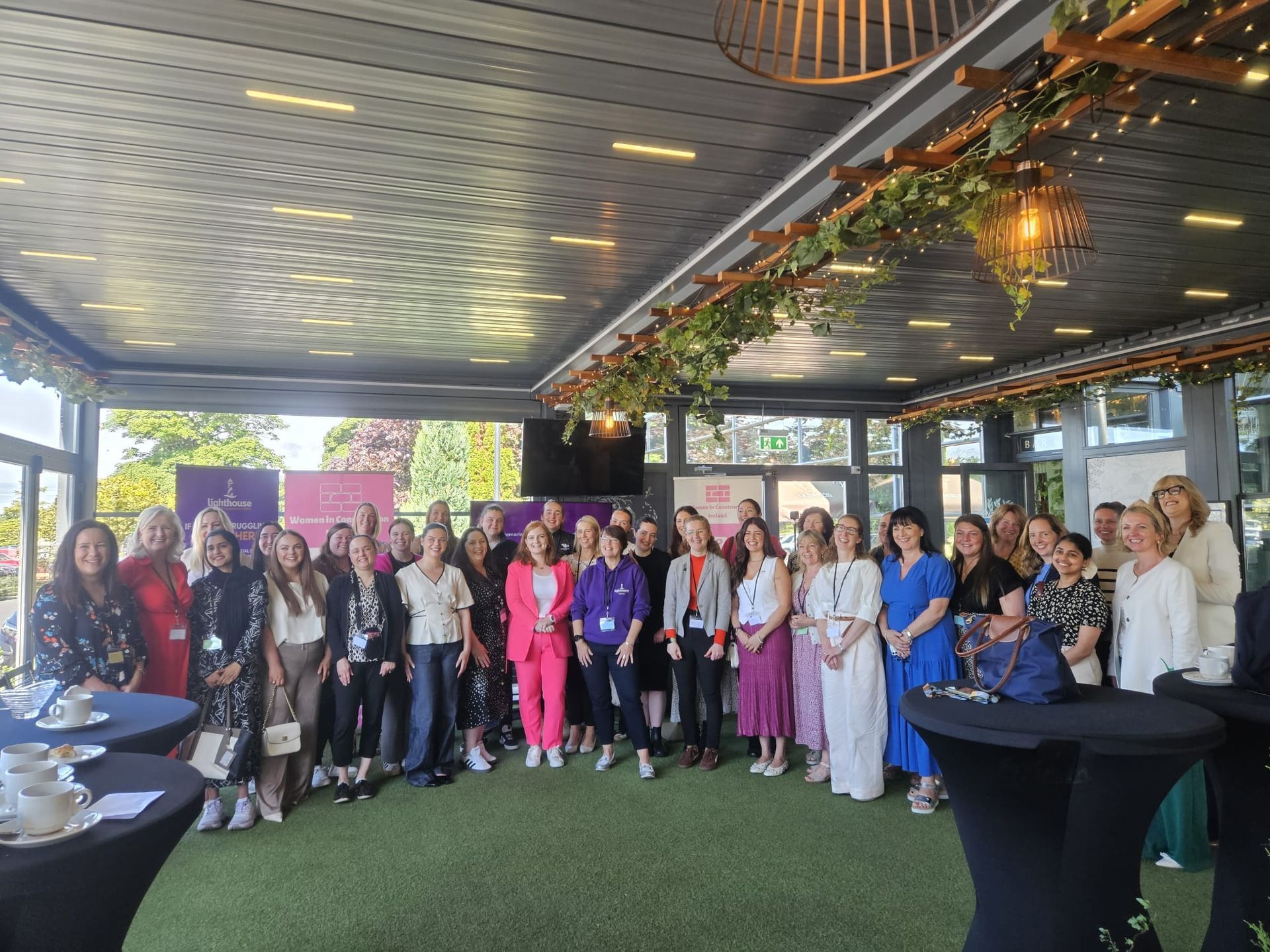 Large group posing for a photo under a covered patio with greenery and tall cocktail tables