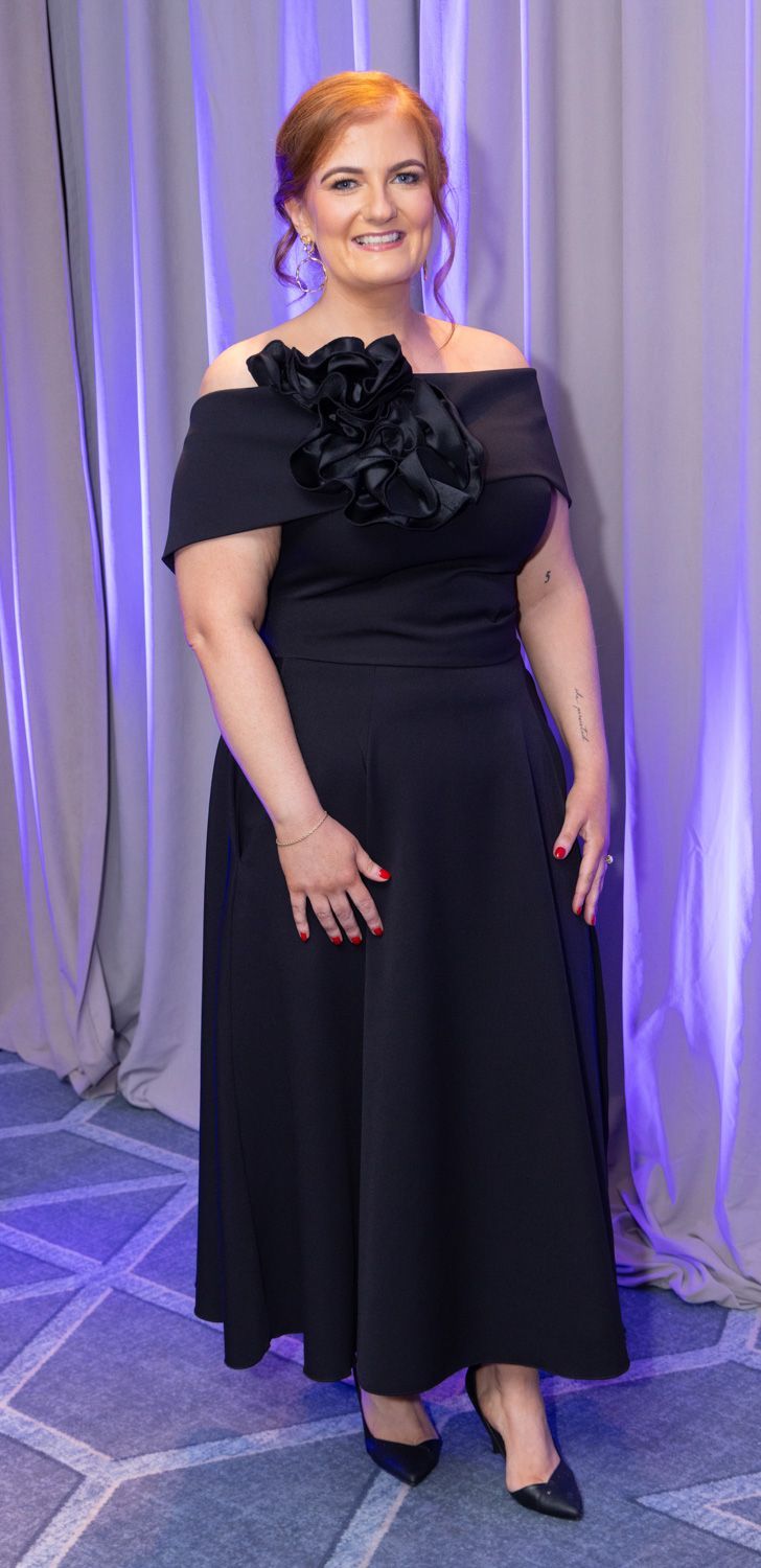 Woman in a black evening gown posing at a purple-lit event backdrop