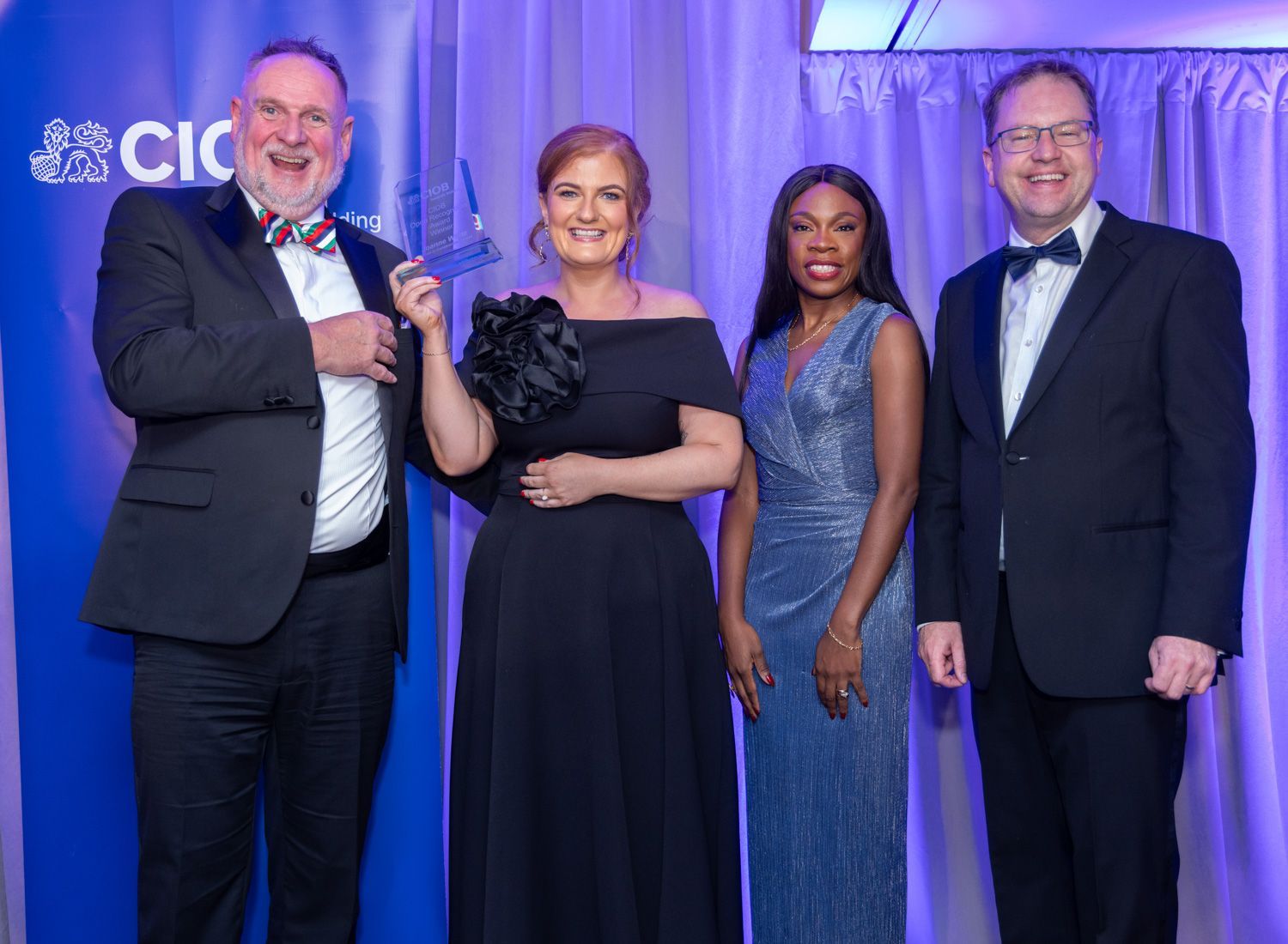 Four people in formal attire pose on a blue-lit stage at a charity or awards event.
