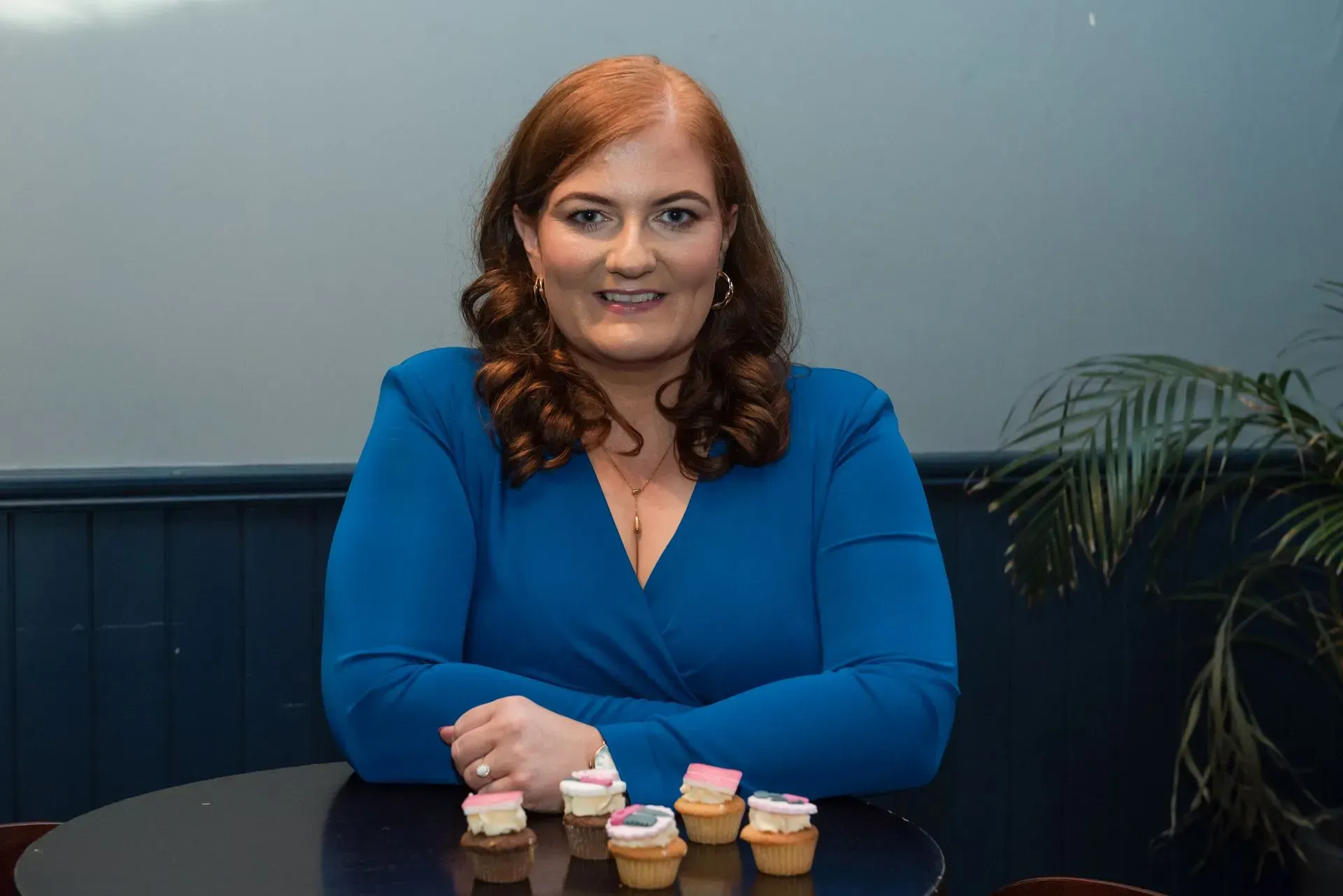 Woman in blue top sitting at a table with small cupcakes in a room