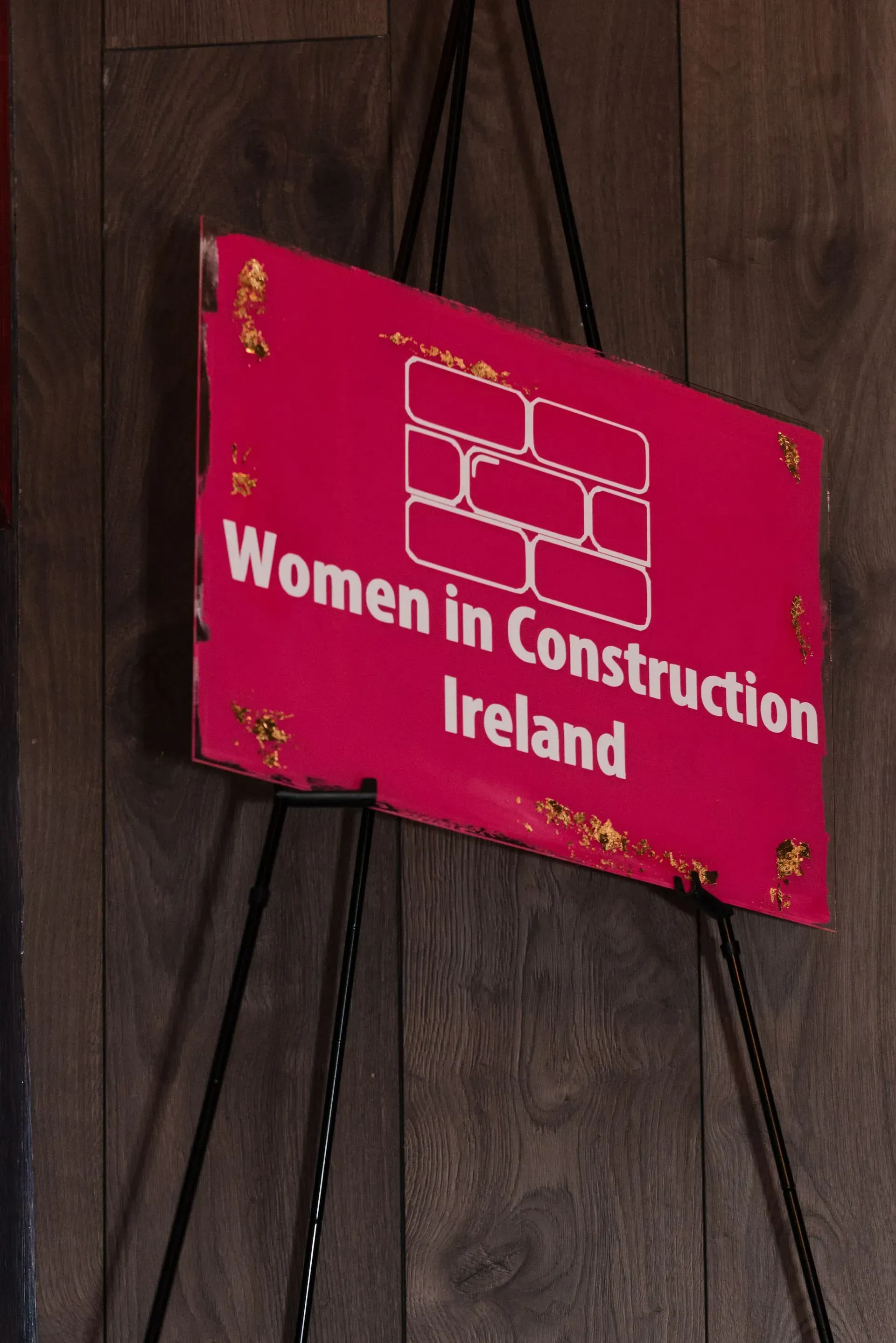Pink sign reading “Women in Construction Ireland” on a wooden wall.