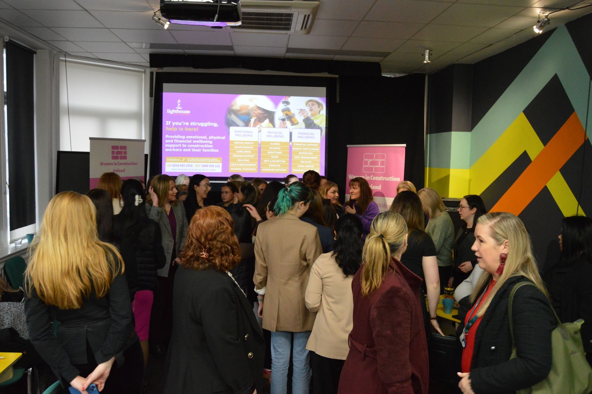 Crowd gathered in a conference room facing a presentation screen with purple slides.
