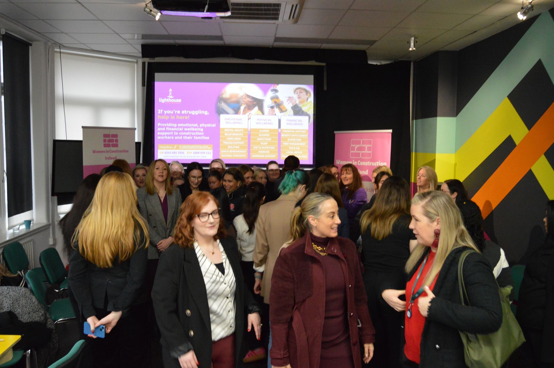 People gathered in a room listening to a presentation on a purple screen.