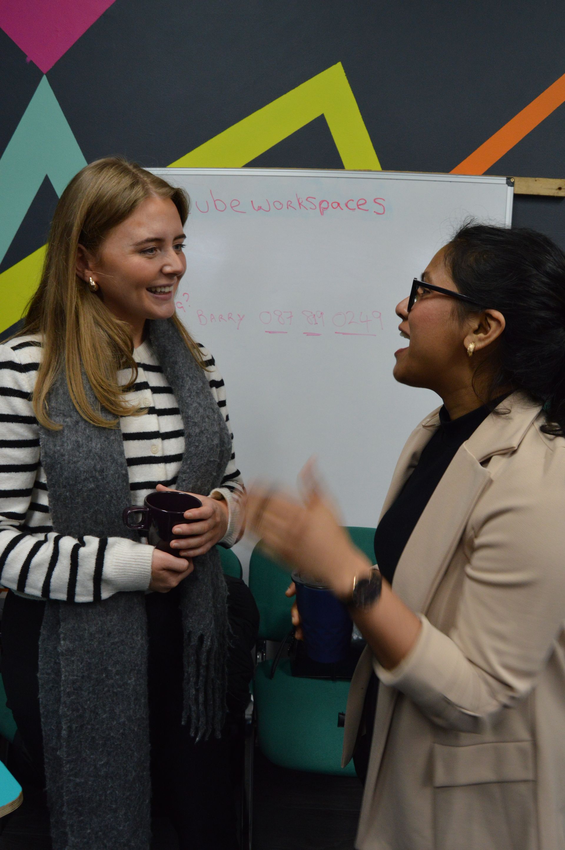Two women chatting in front of a whiteboard in a colorful office space