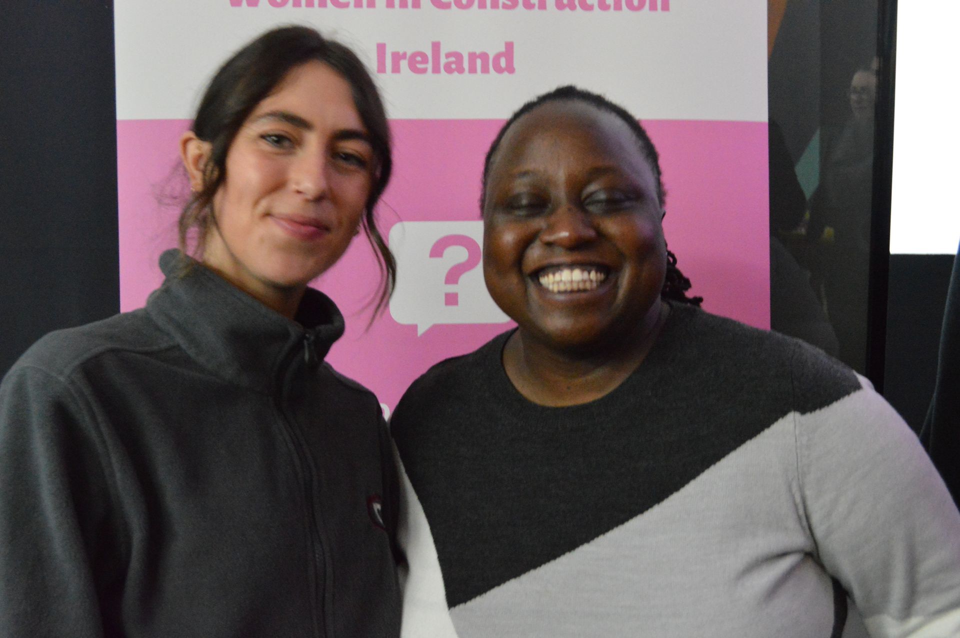 Two smiling people standing together in front of a pink conference banner.
