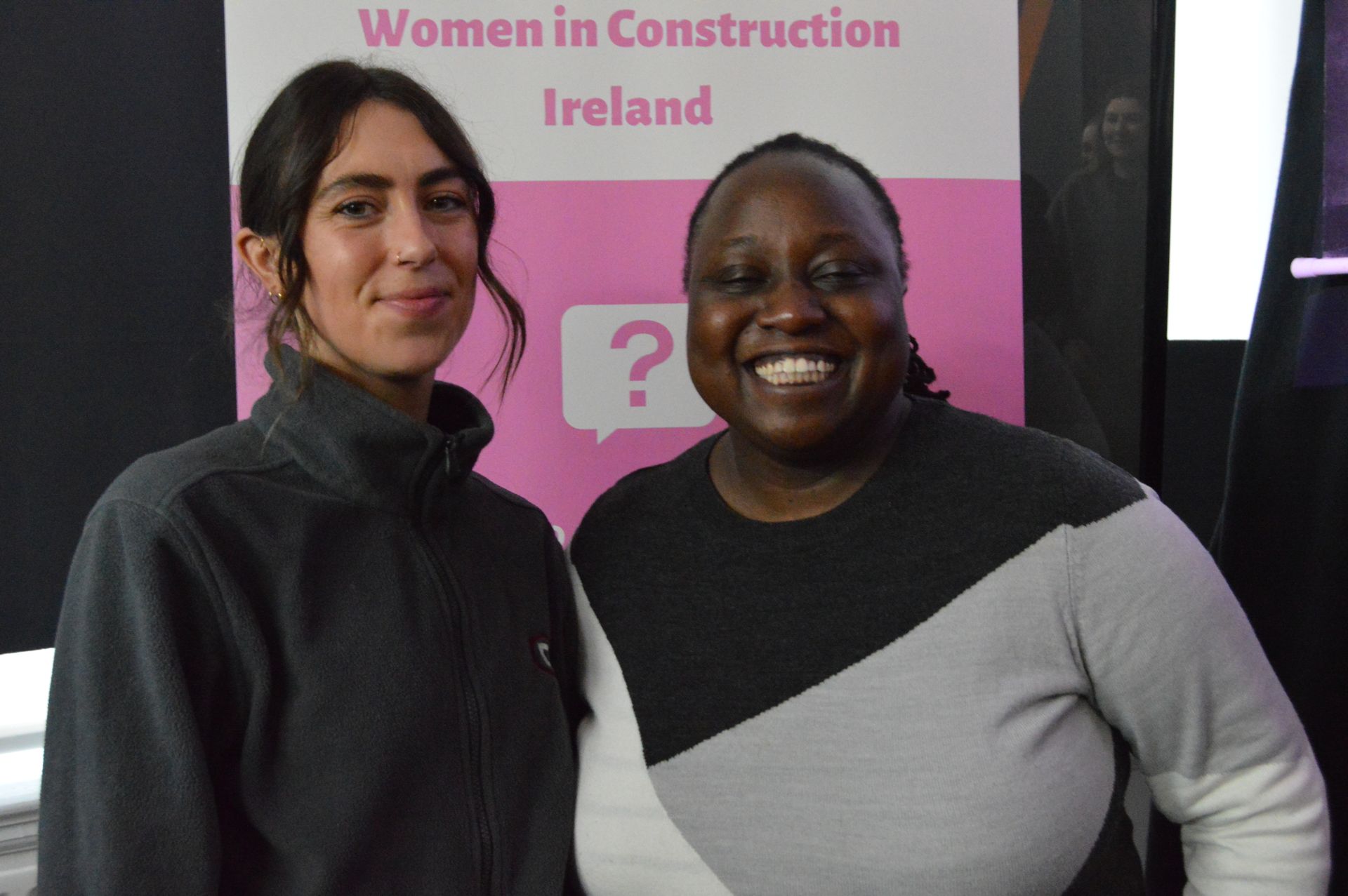 Two people standing in front of a Women in Construction Ireland banner, smiling.