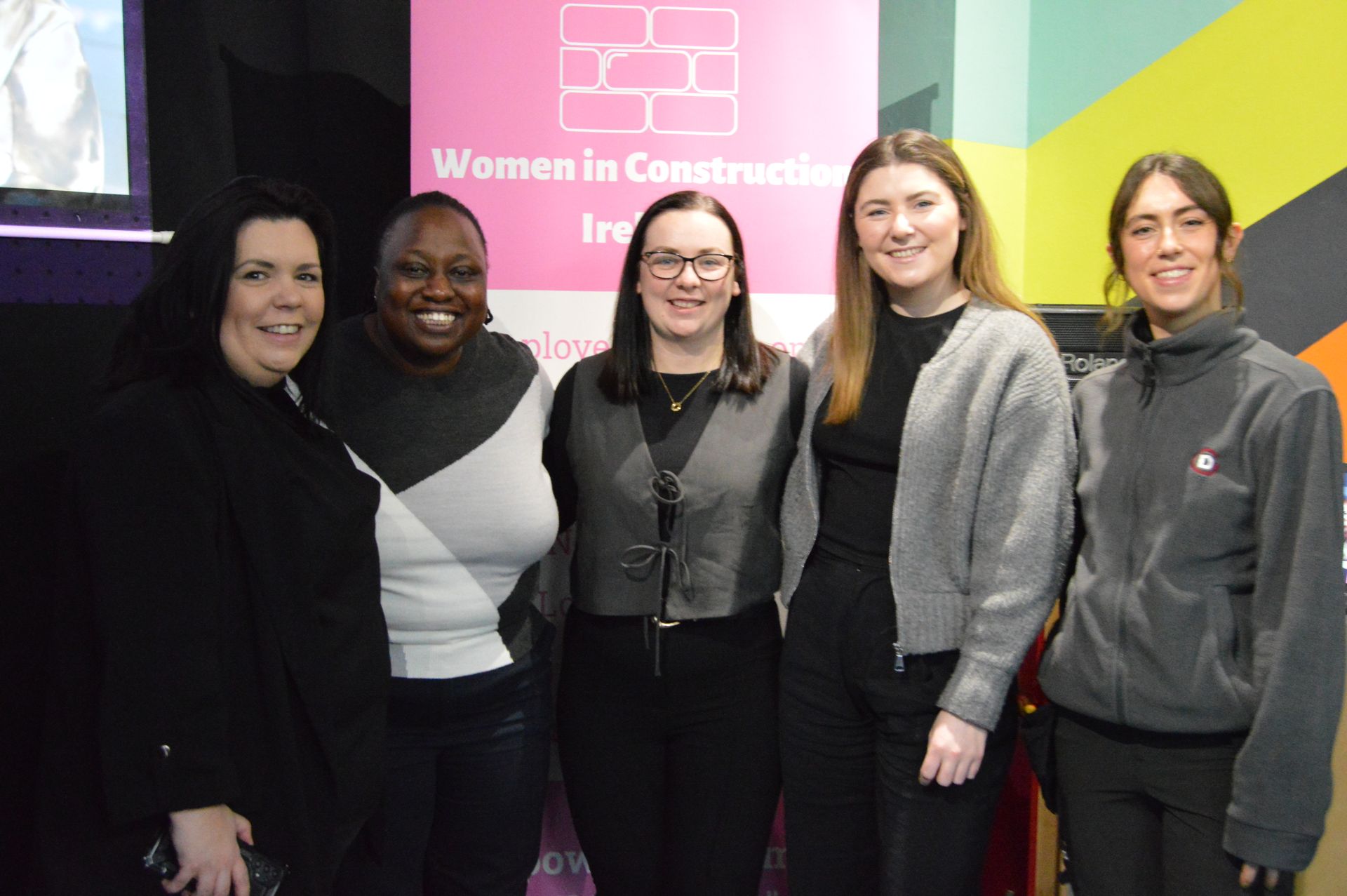 Five people standing together in front of a colorful Women in Leadership conference backdrop