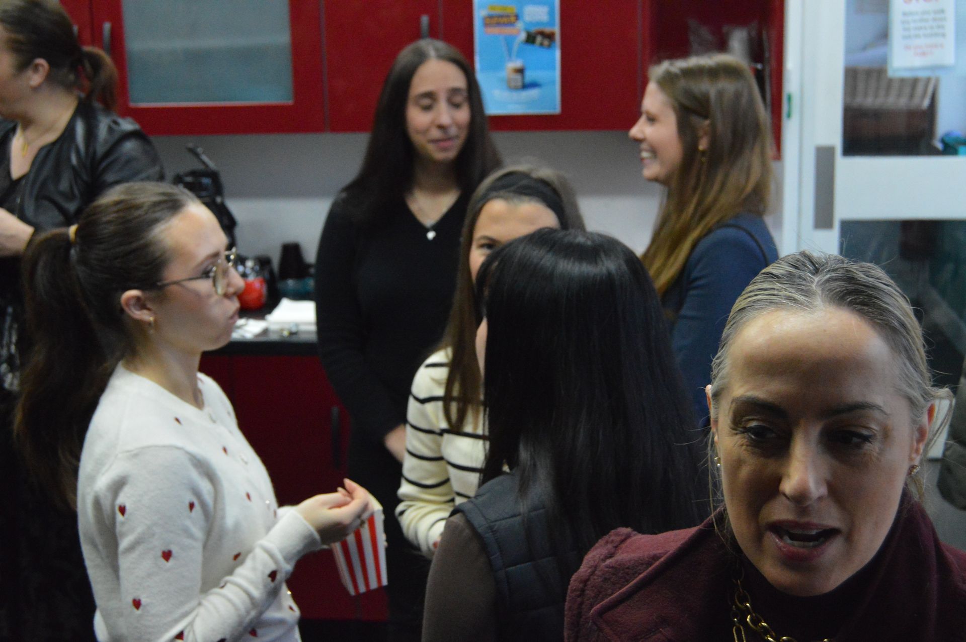 Several people chatting in a room; one woman in the foreground looks toward the camera.