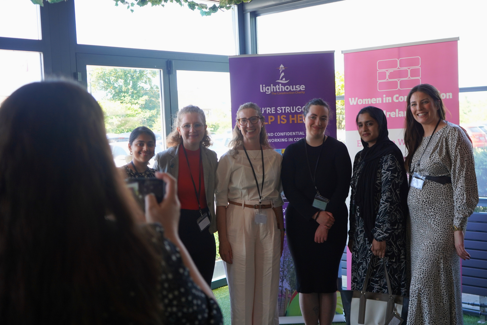 Group posing for a photo beside a purple event banner in a bright indoor lobby.