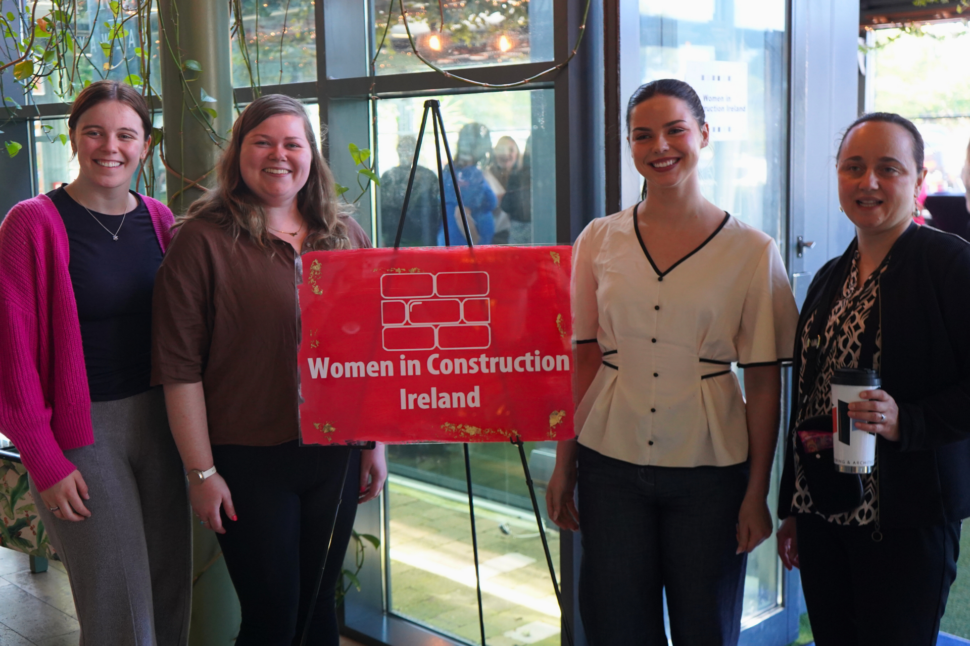 Four people stand beside a red “Women in Construction Ireland” sign in a bright lobby.
