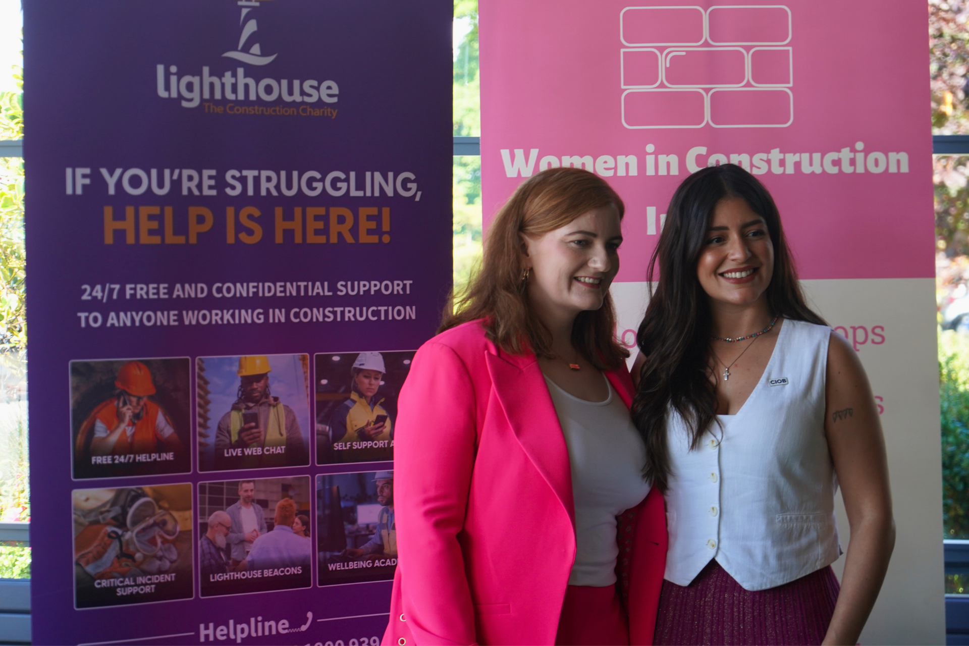 Two women smiling in front of a Women in Construction and Lighthouse help poster