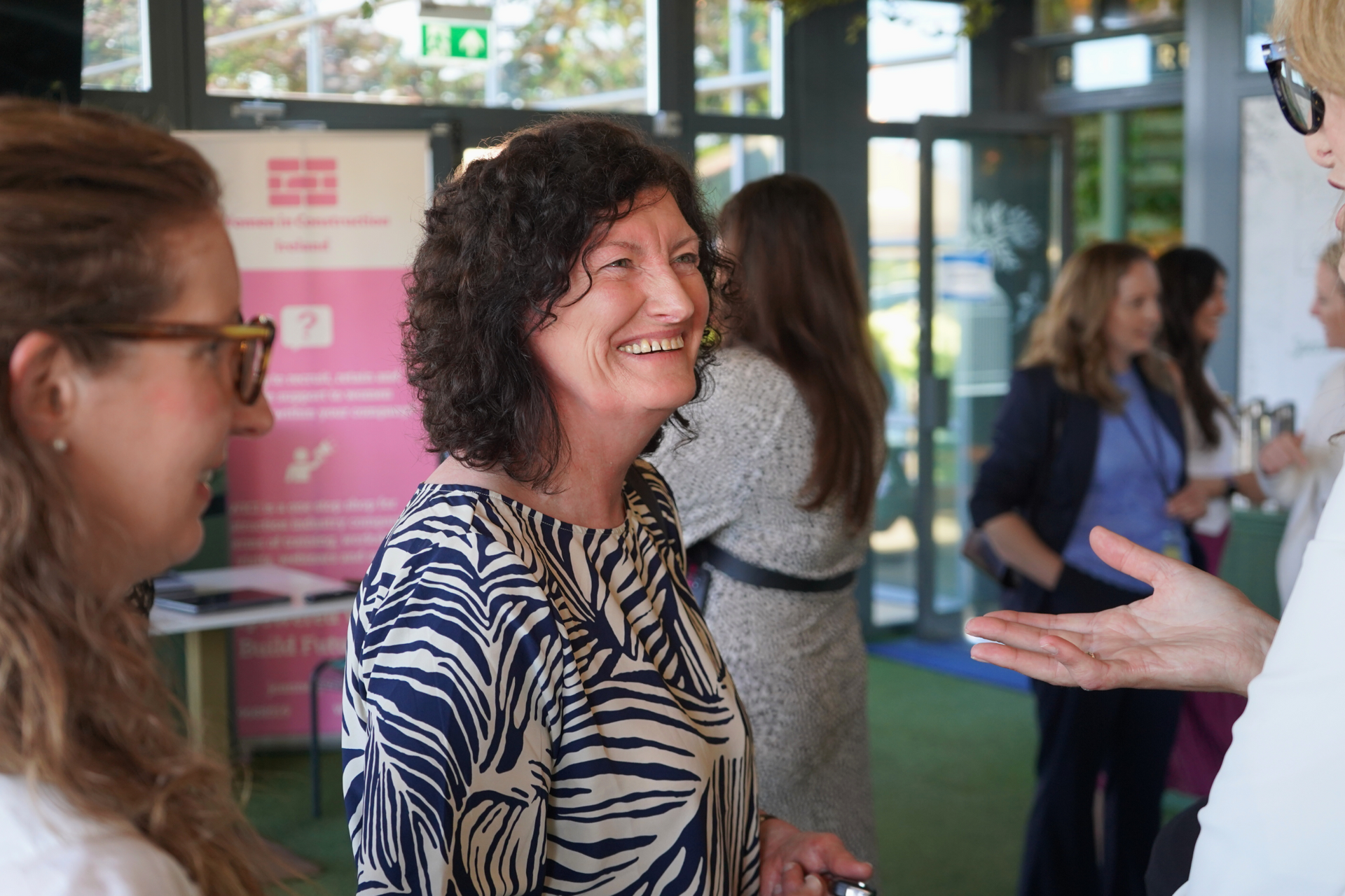 People chatting at an indoor event, smiling near a table and posters.
