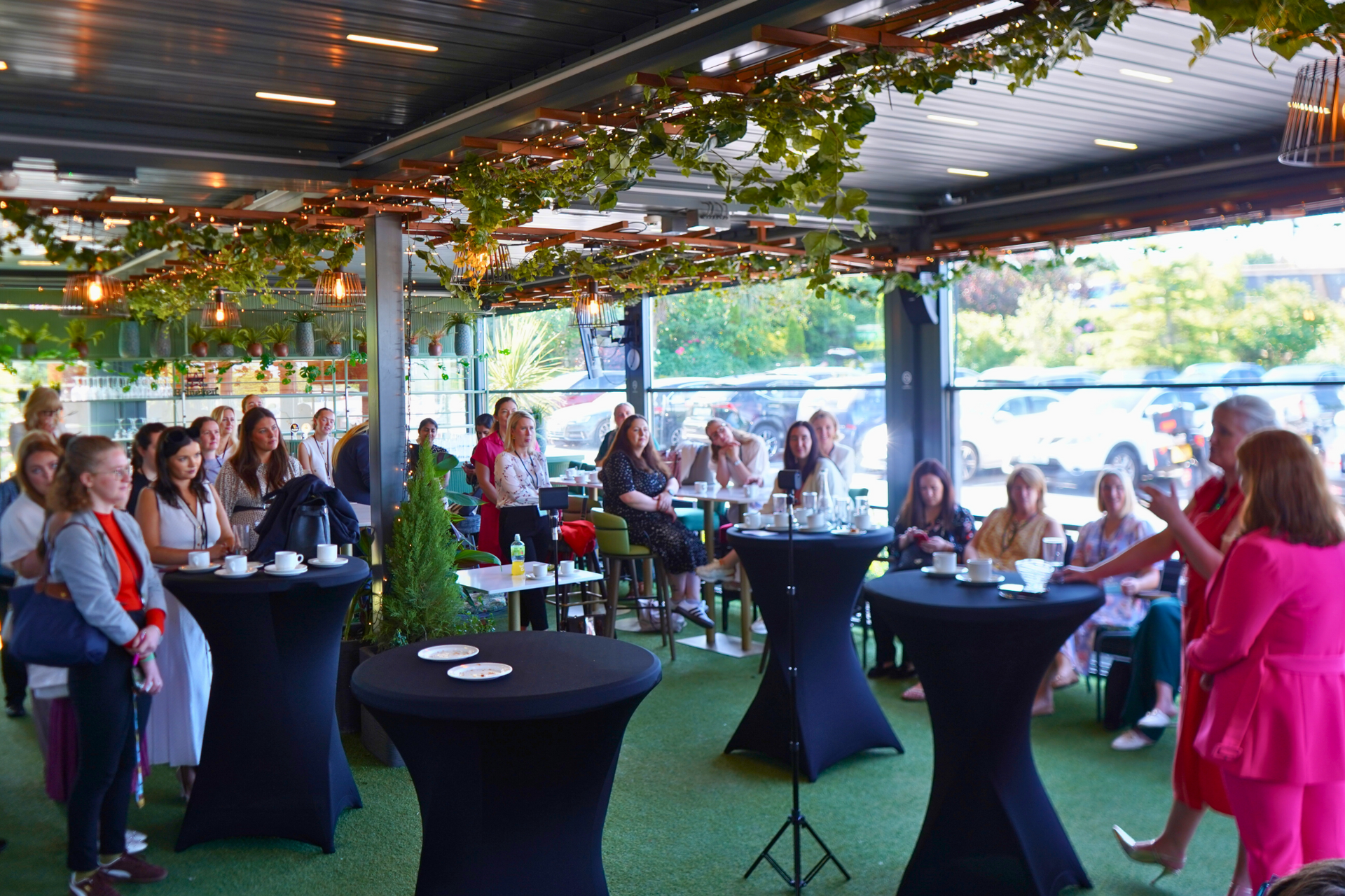 Guests mingling at a covered outdoor event with cocktail tables and a woman in a bright pink dress