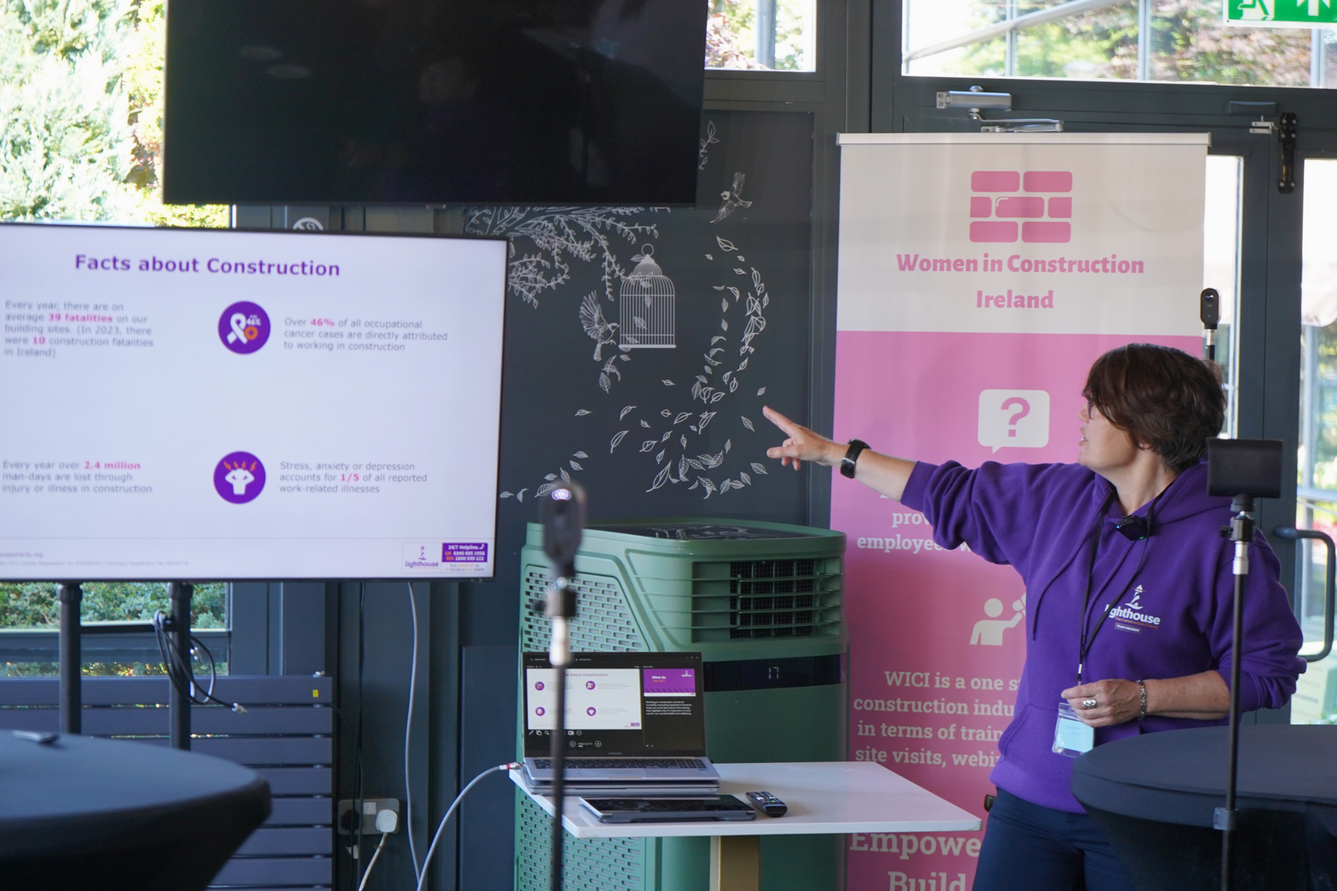 Person in purple pointing at a presentation screen in a meeting room