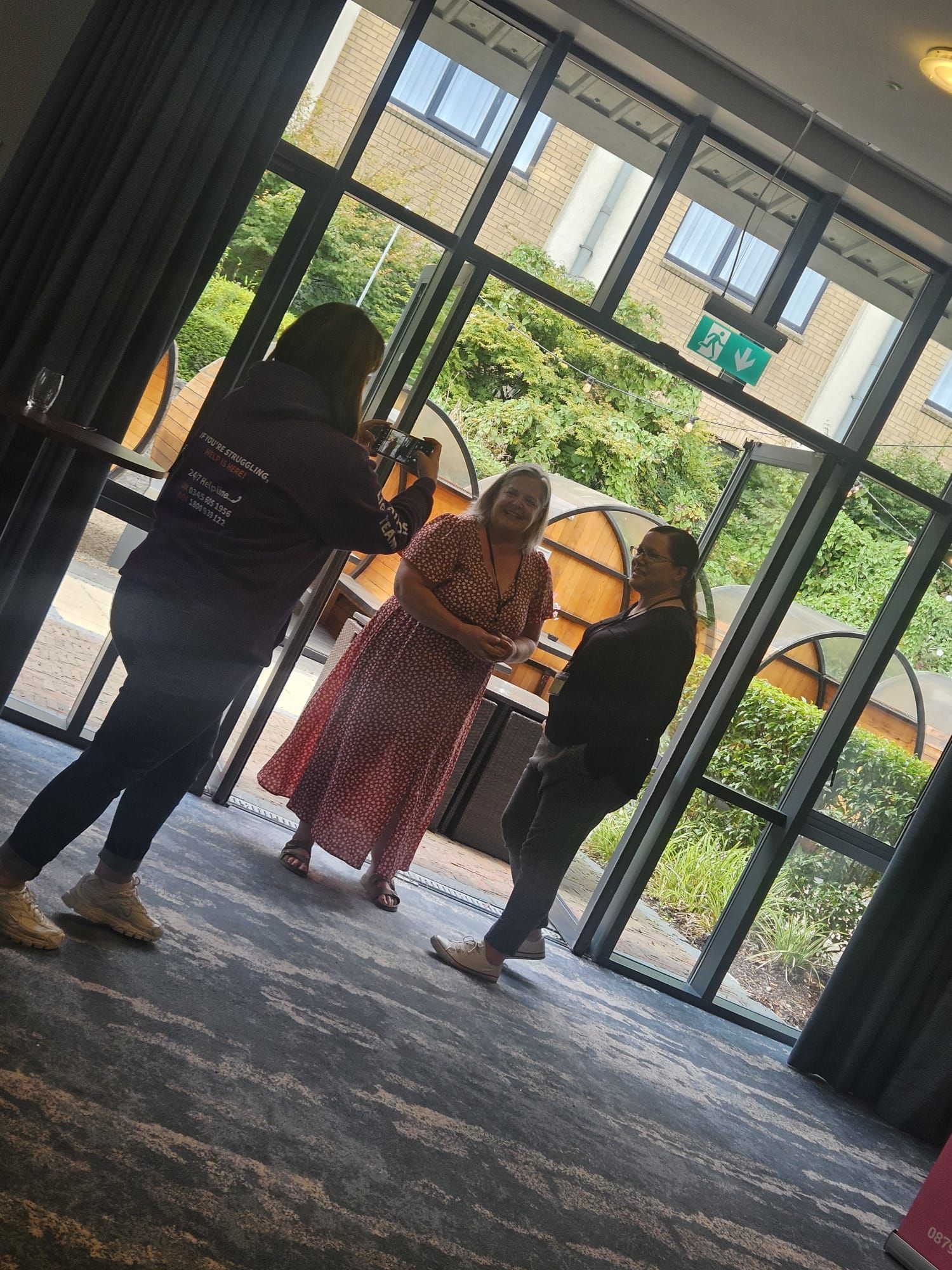 Three people standing in a lobby near glass doors, with a large umbrella and plants outside.
