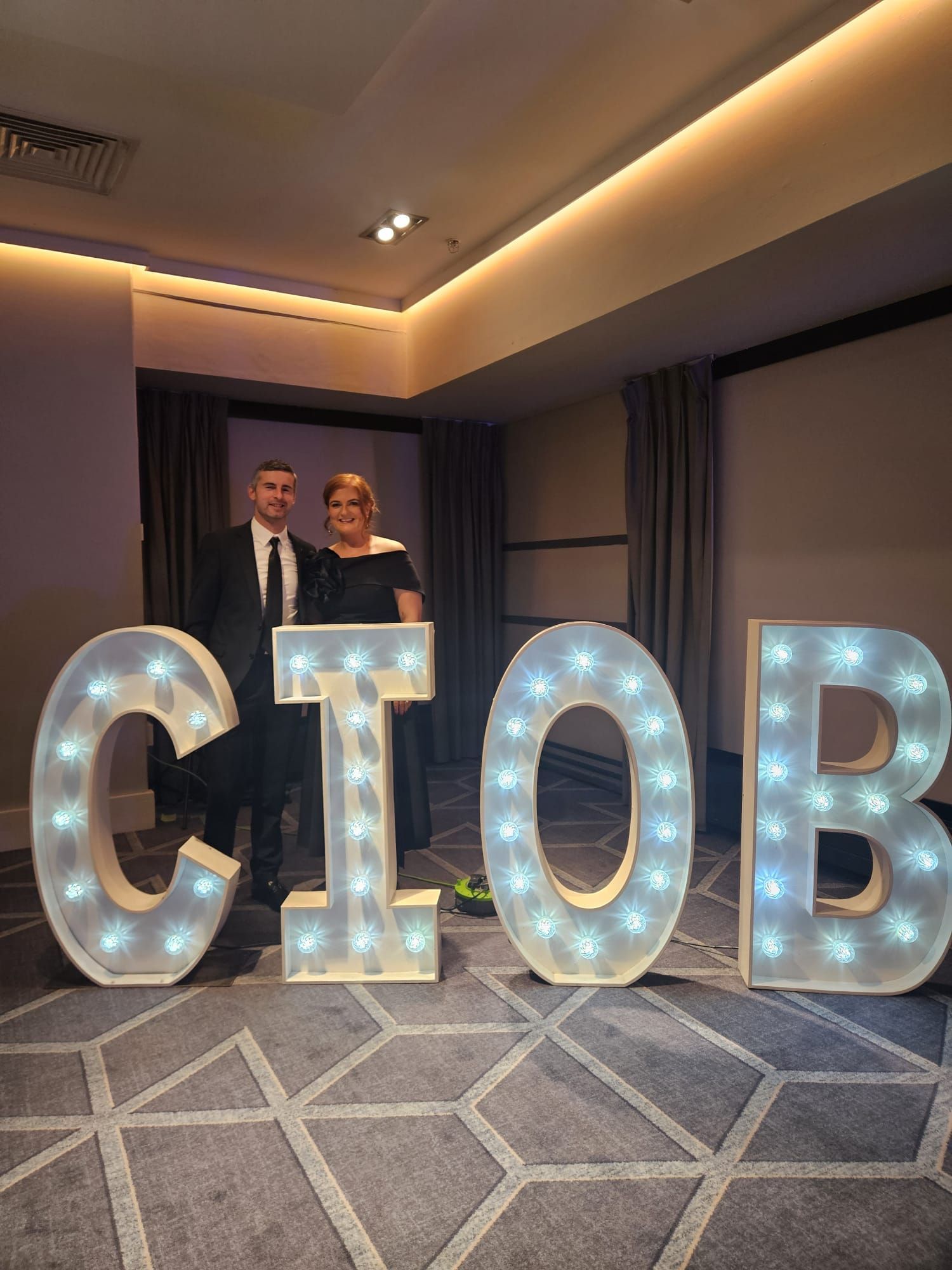 Two people standing beside large illuminated letters spelling CLOB in a hotel ballroom