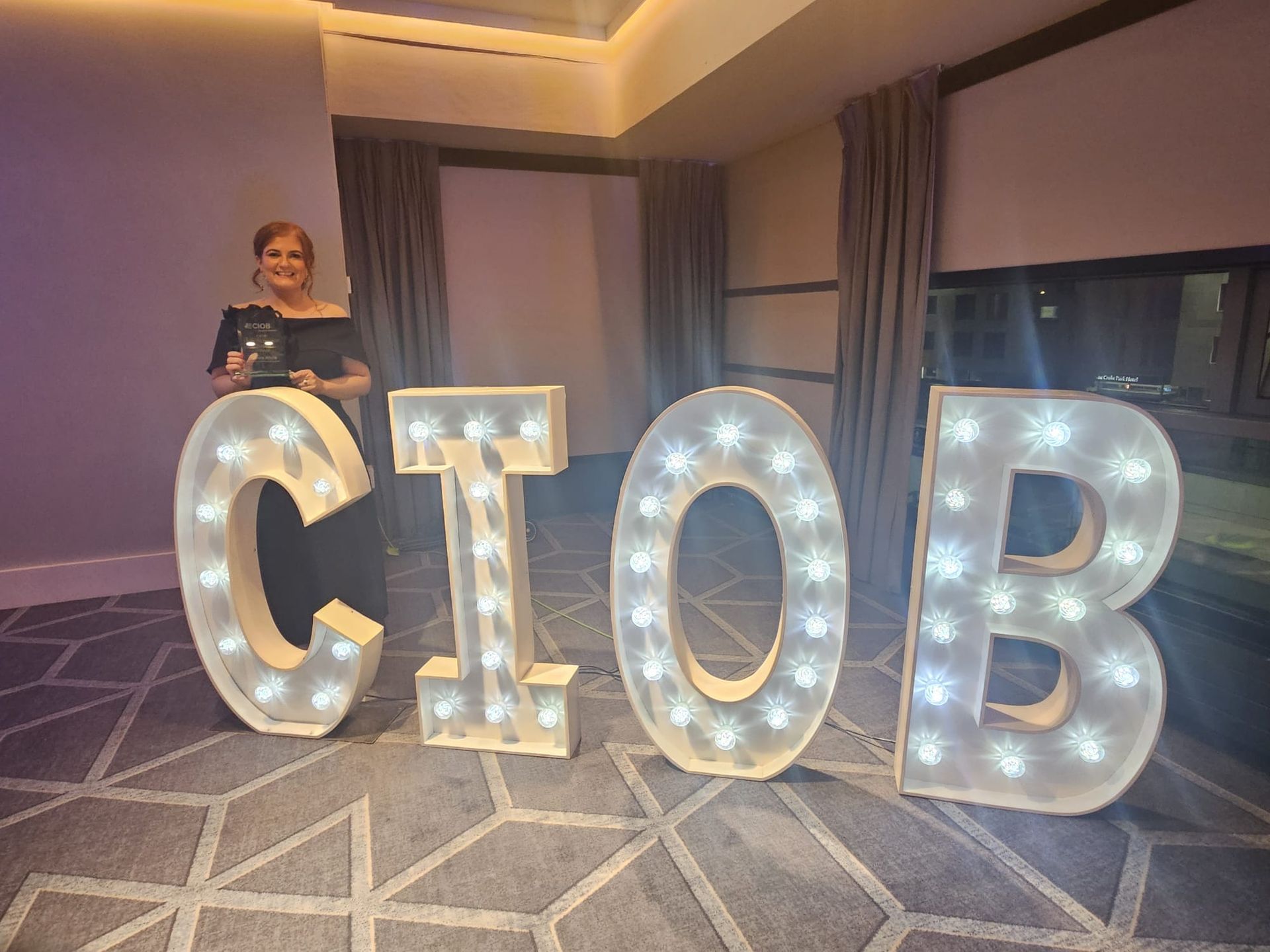Woman standing behind large illuminated “CIOB” letters in a banquet hall.