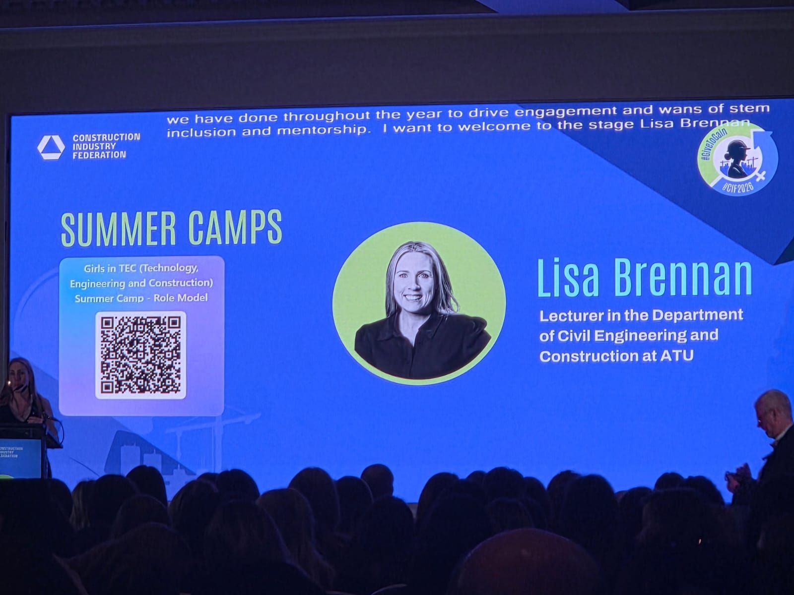 Blue conference slide showing Lisa Brennan, a QR code, and “Summer Camps” text with audience silhouettes below