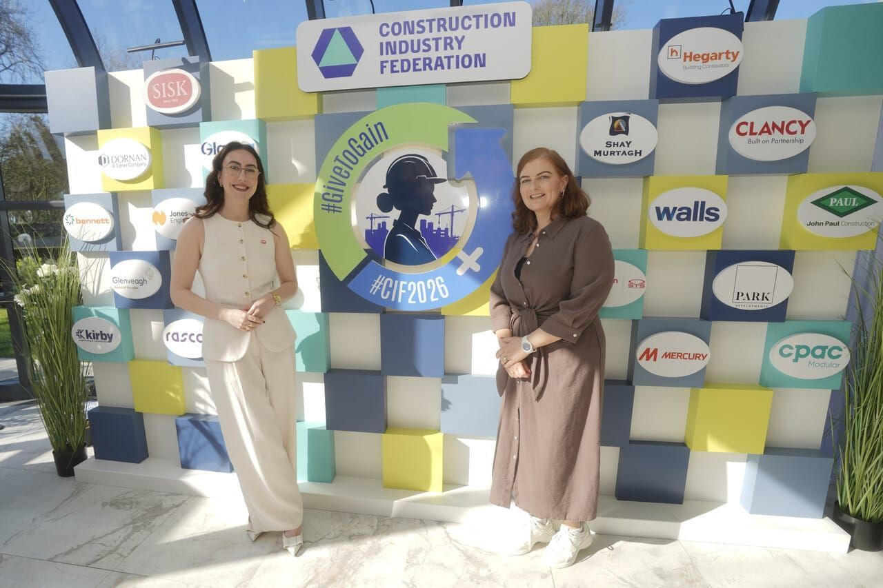 Two people posing before a Construction Industry Federation event backdrop with logo wall and blue-white décor