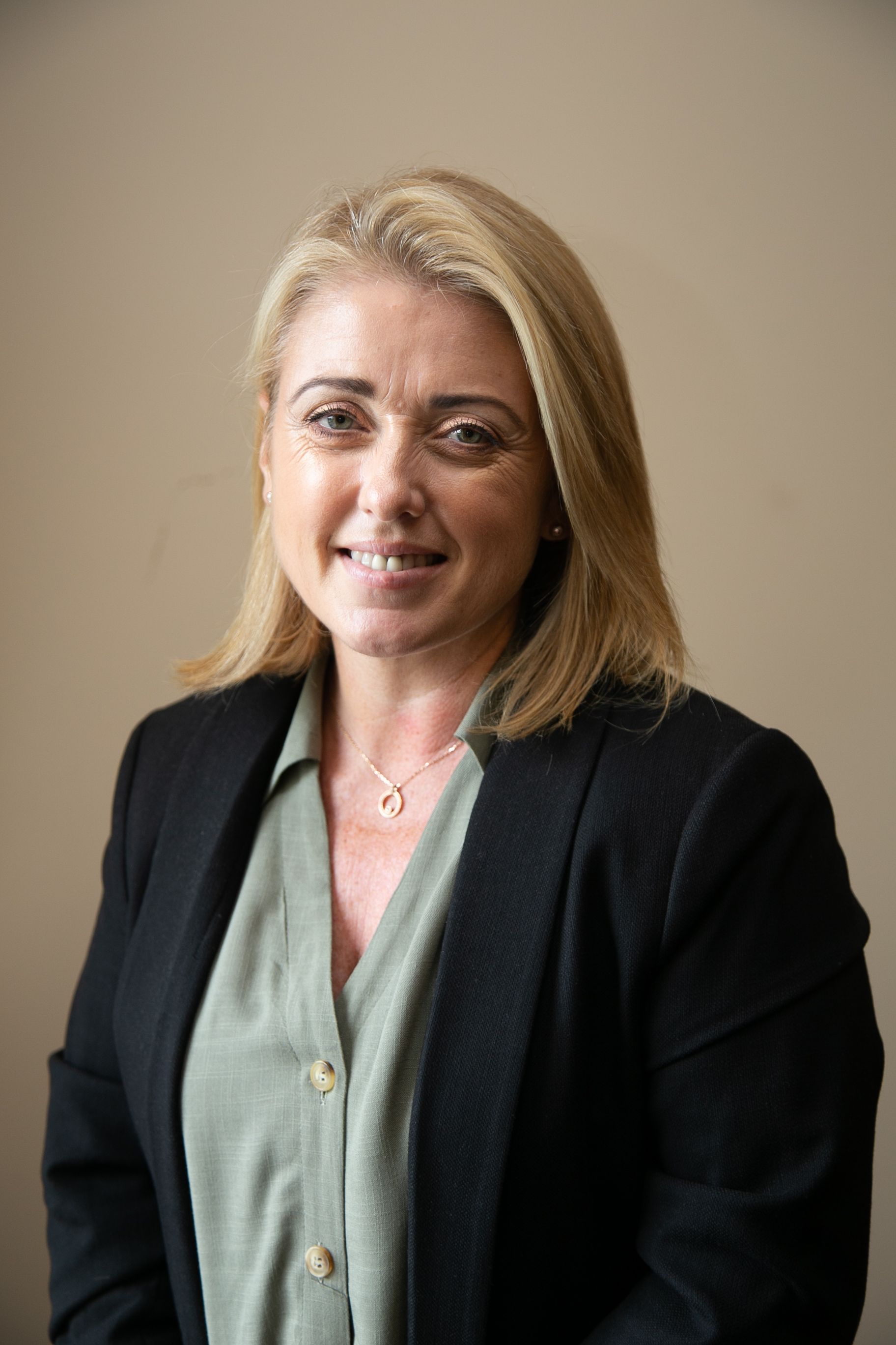 Portrait of a smiling woman in a black blazer and green blouse against a plain background