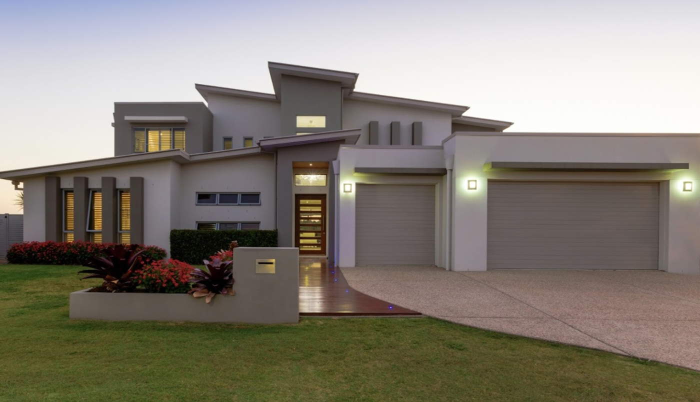 Modern two-story house with gray and white exterior, two-car garage, and lush green lawn.