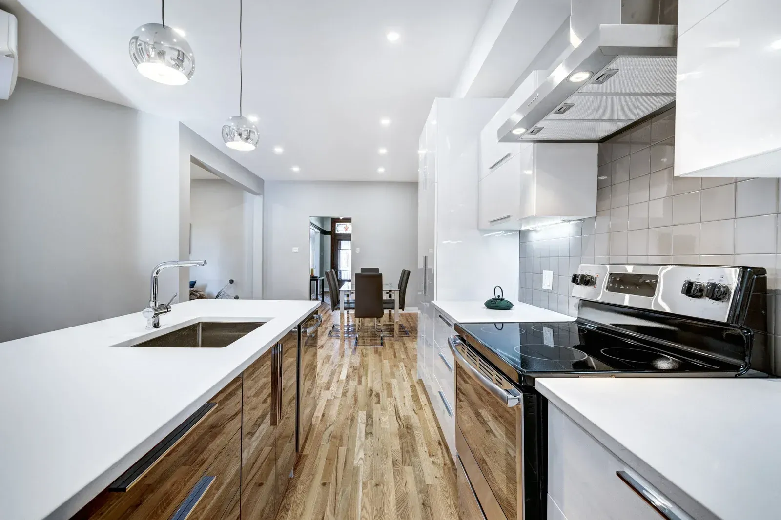 Modern kitchen with white countertops, stainless steel appliances, and wooden floors.