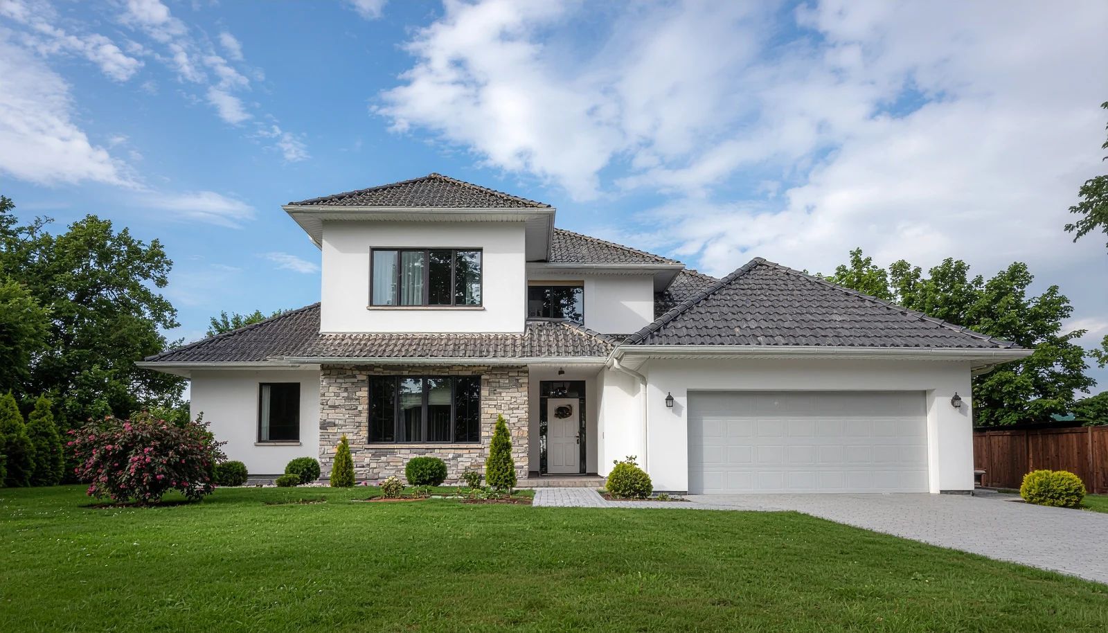 Modern two-story white house with gray trim, black garage door, and landscaped front yard