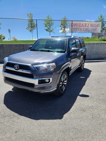 A gray toyota 4runner is parked in front of a fence.