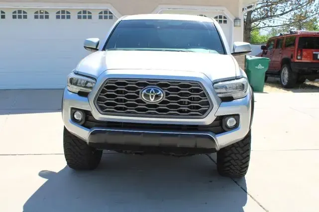 A silver toyota tacoma truck is parked in a driveway in front of a garage.