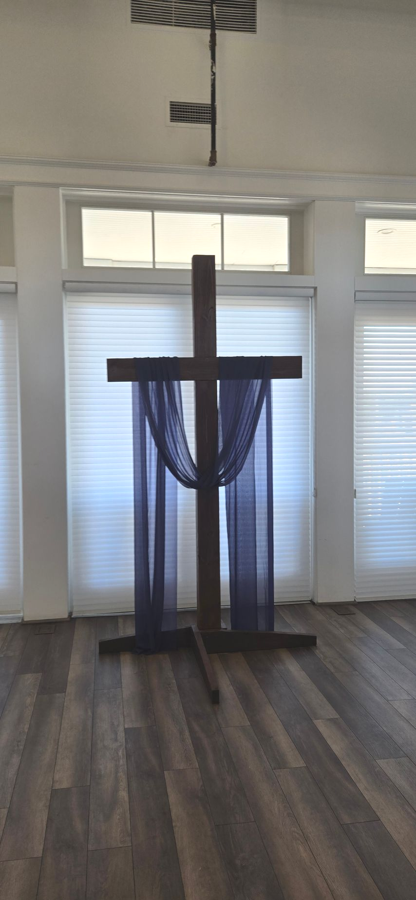 Wooden cross with draped blue fabric in a bright room with windows and hardwood floor