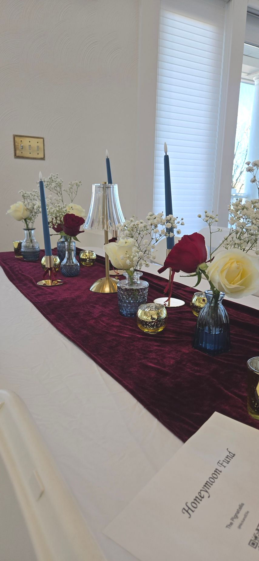 Decorated banquet table with red cloth, candles, flowers, and glassware in a bright room