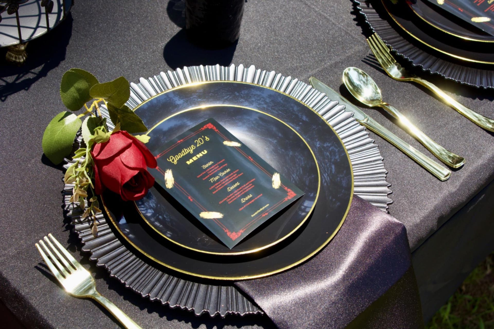 Elegant black-and-gold plate with red rose and silver utensils on a tablecloth