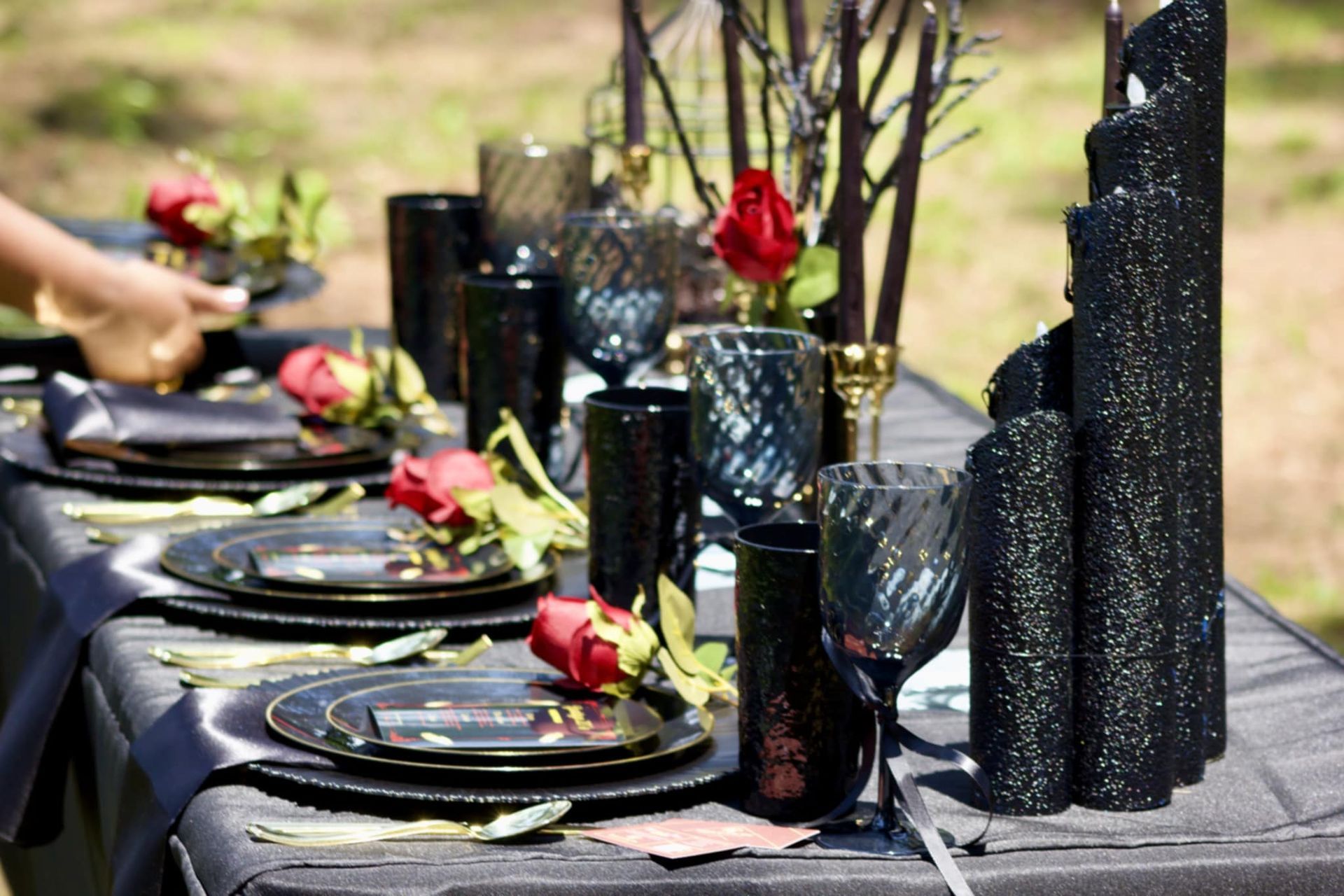 Black and gold outdoor table setting with plates, glasses, and red rose centerpieces