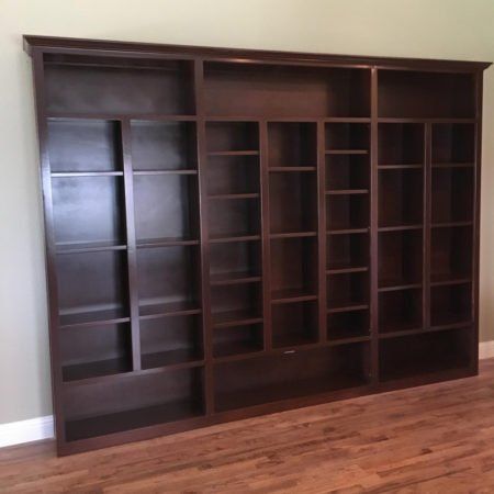 Dark wood wall unit with shelves and cubbies in an empty room with hardwood floors