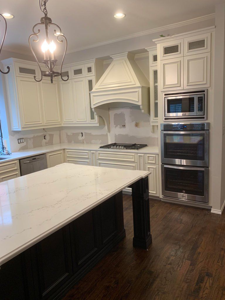 Elegant white kitchen with marble island, dark wood floor, and double wall ovens