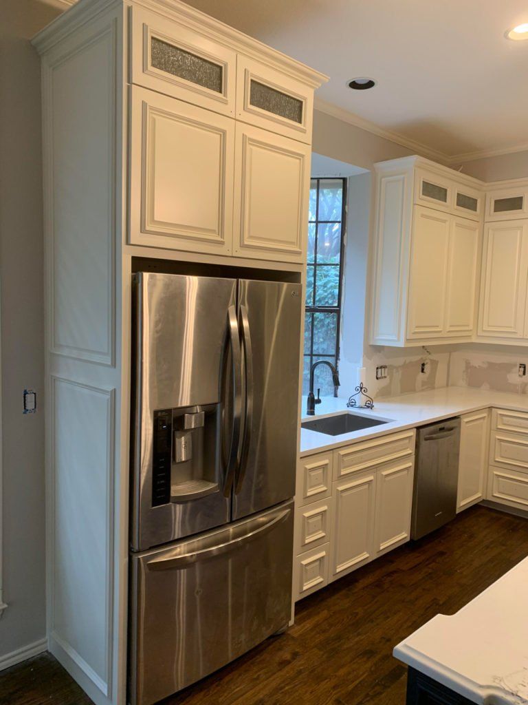 Bright modern kitchen with stainless steel fridge, white cabinets, and dark wood floors.